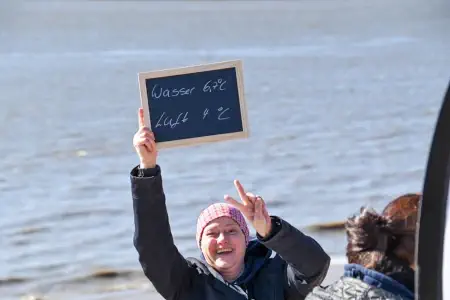 Frau am Strand hält Schild mit Info der Badetemperatur im Maerz hoch
