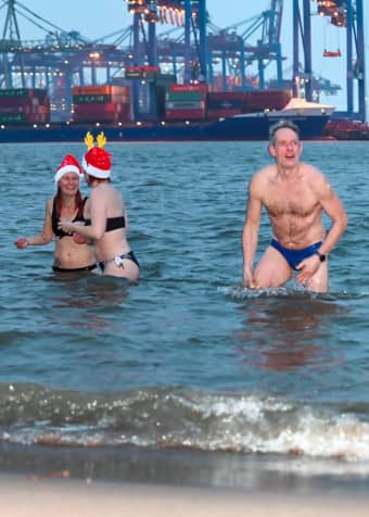 zwei junge Frauen ermutigen sich gegenseitig ins kalte Wasser einzutauchen. Ein ältere Mann hat es bereits hinter sich gebracht