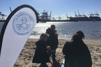 Banner der Eisbademeisters mit Personen am Strand von Hamburg
