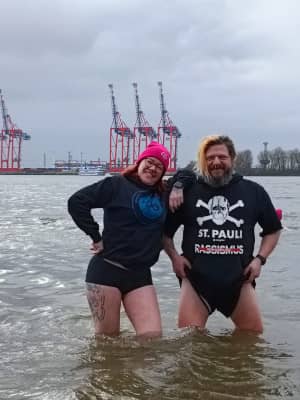 Mann und Frau mit kurzer Hose und langem Shirt stehen bis zu den Knien im kaltem Flusswasser
