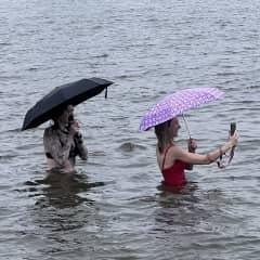 zwei Frauen mit Regenschirm und Badeklamotte im Wasser