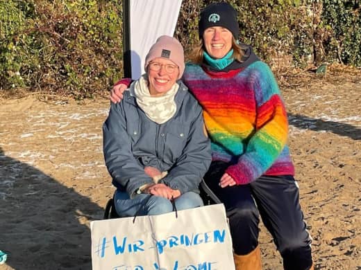 Frau im Rollstuhl mit Begleitung am Strand