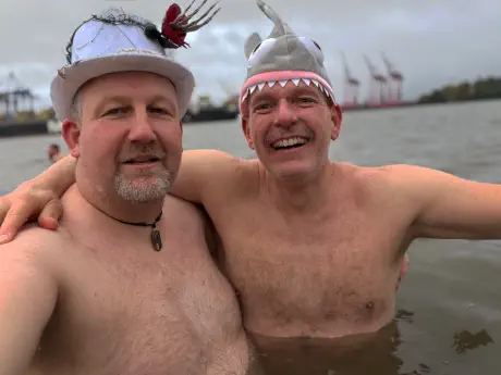 Zwei Männer präsentieren ihre Kopfbedeckung (silberner Hut und eine Haimütze)