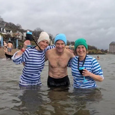 Zwei Eisbadefrauen im blau-weißen Anzug stehen mit einem Kaltbader in der 9,4 Grad kalten Elbe.