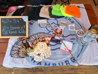 Tisch mit Mützen, Flyern und einem Hinweisschild (9,4 Grad Wassertemperatur, Eisbaden für die Offroad Kids)