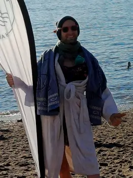 Mann mit Sonnenbrille, Mütze und im Bademantel steht neben dem Aufsteller der Eisbademeisters Hamburg