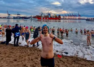 euphorischer Eisbader am Strand mit weiteren Menschen, die ins eisige Wasser gehen.