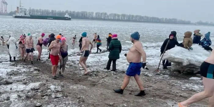 Menschen folgen der Schneise im Sand, die befreit von Eis befreit ist, um in den Fluss baden zu gehen.