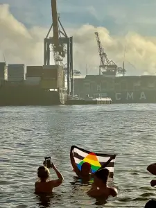 Eisbader in der Elbe und hält eine Regenbogenflagge hoch