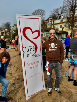 Neben Cafeé mit Herz Banner steht ein Mann.